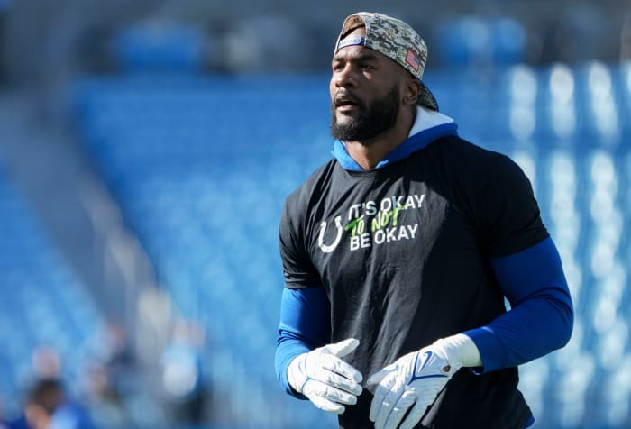Shaq Leonard looks ahead walking on the field with gloves on wearing a shirt that says “It’s okay to not be okay”
